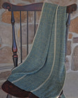 The handwoven blue and green scarf draped over a chair with a stone wall in the background.