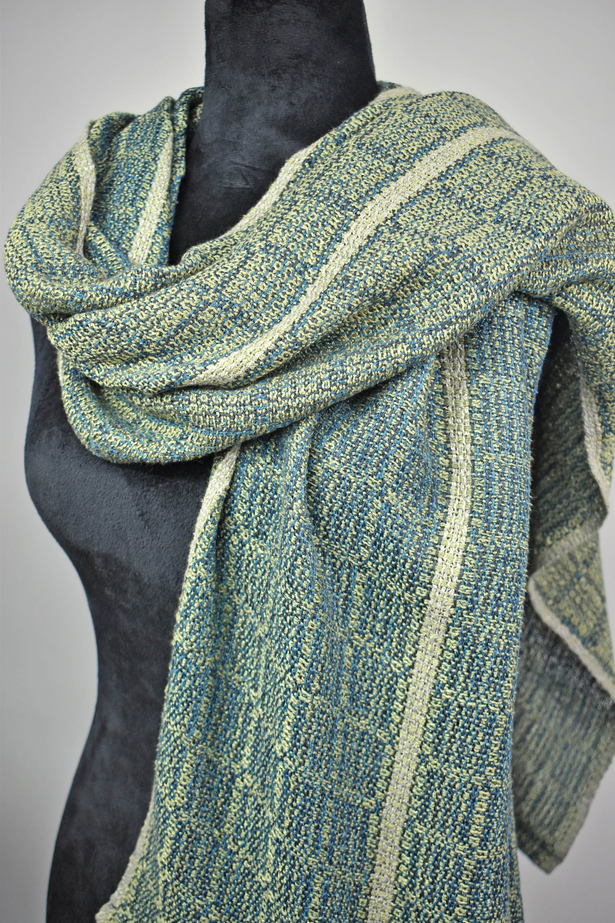 Women's handwoven blue and green scarf styled on a mannequin.