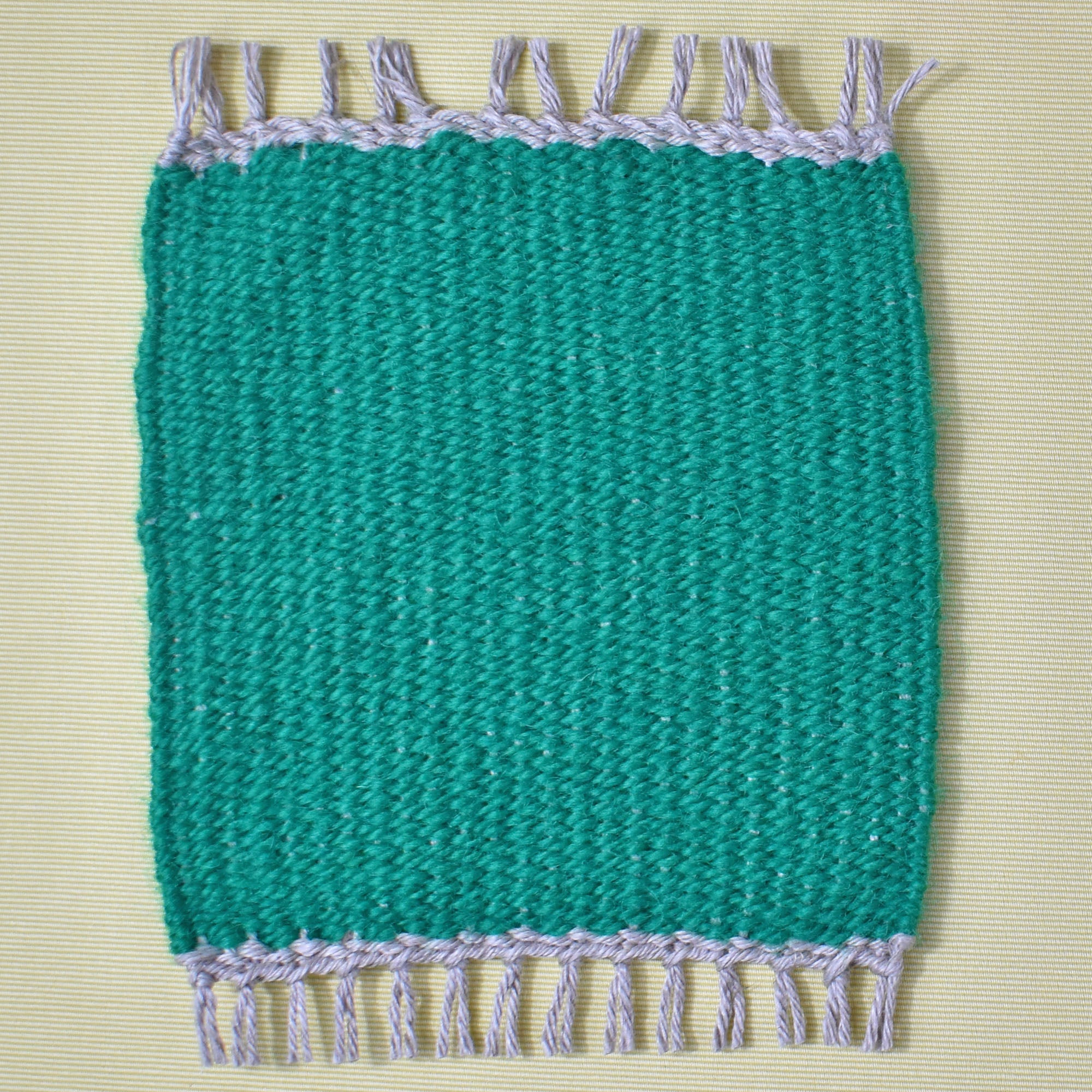 Handwoven mug rug in a solid green color placed on a yellow table.