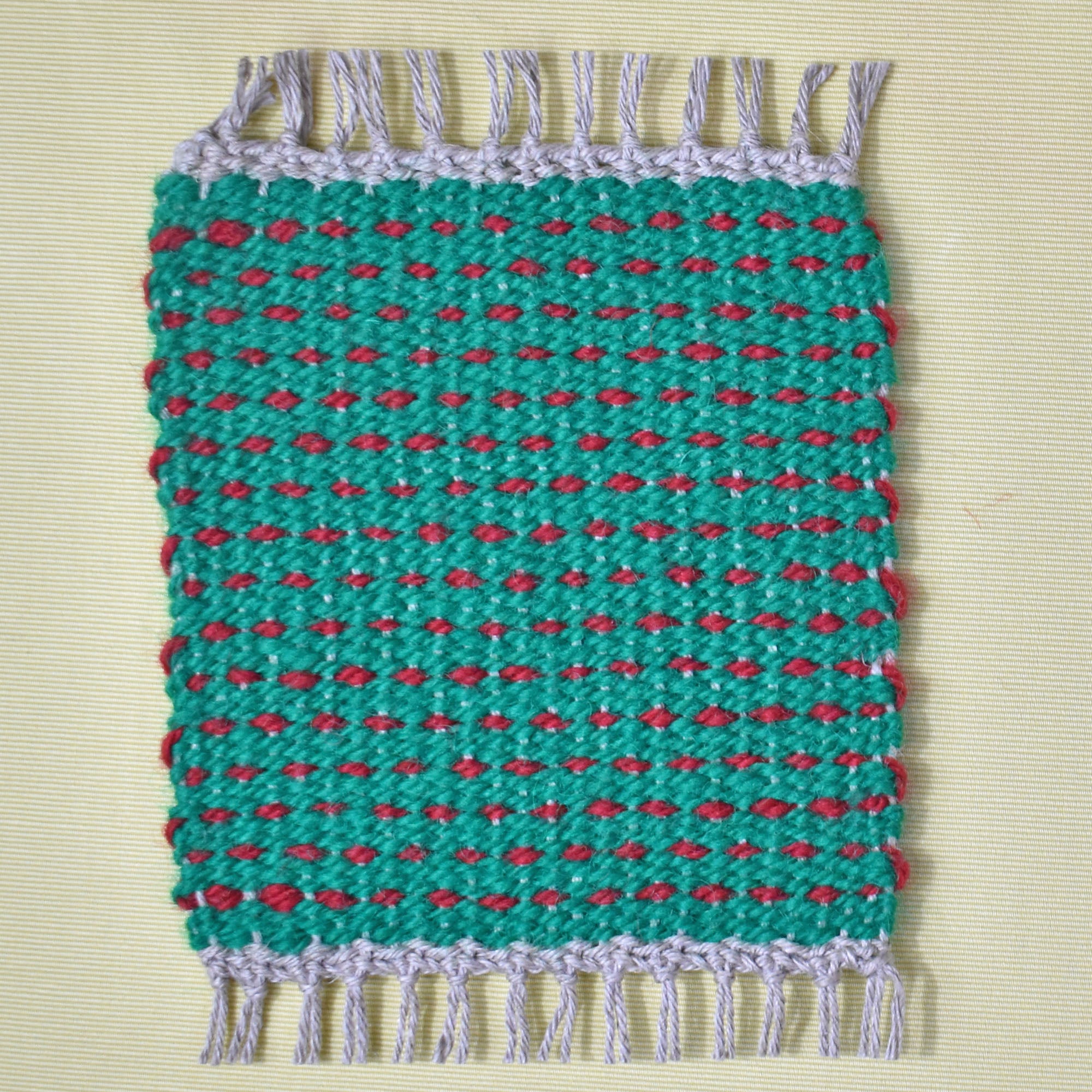 Green mug rug with red dots laying on a white table.