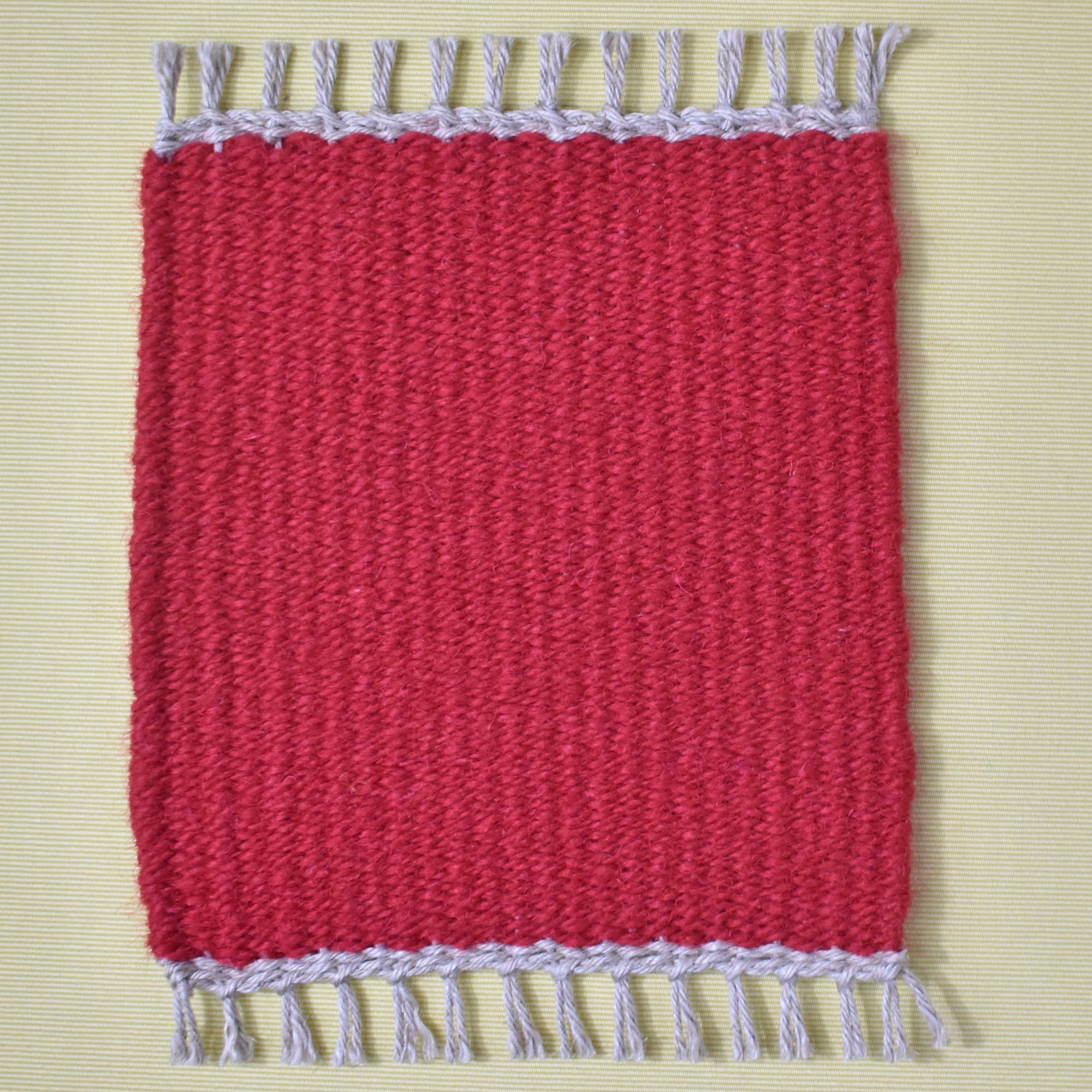 Solid red handwoven mug rug placed on a yellow table.