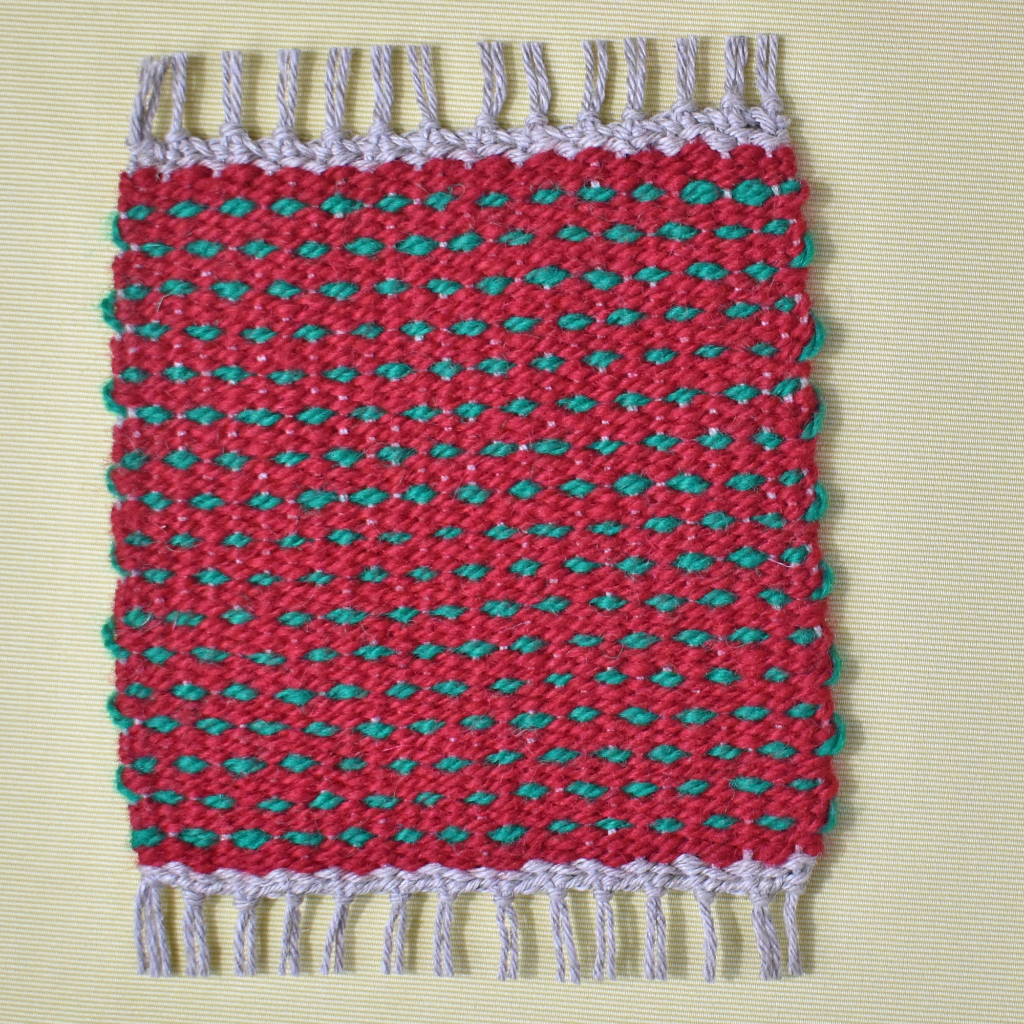 Red with green dots handwoven mug rug on a yellow table.