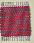 Red with green dots handwoven mug rug on a yellow table.