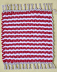 Red and white striped handwoven mug rug laying on a yellow table.